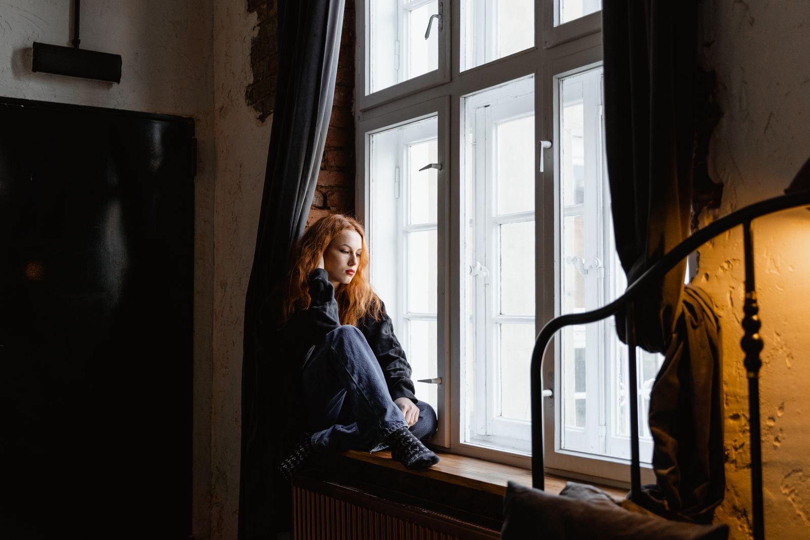 A woman sitting alone by a window in a dim room