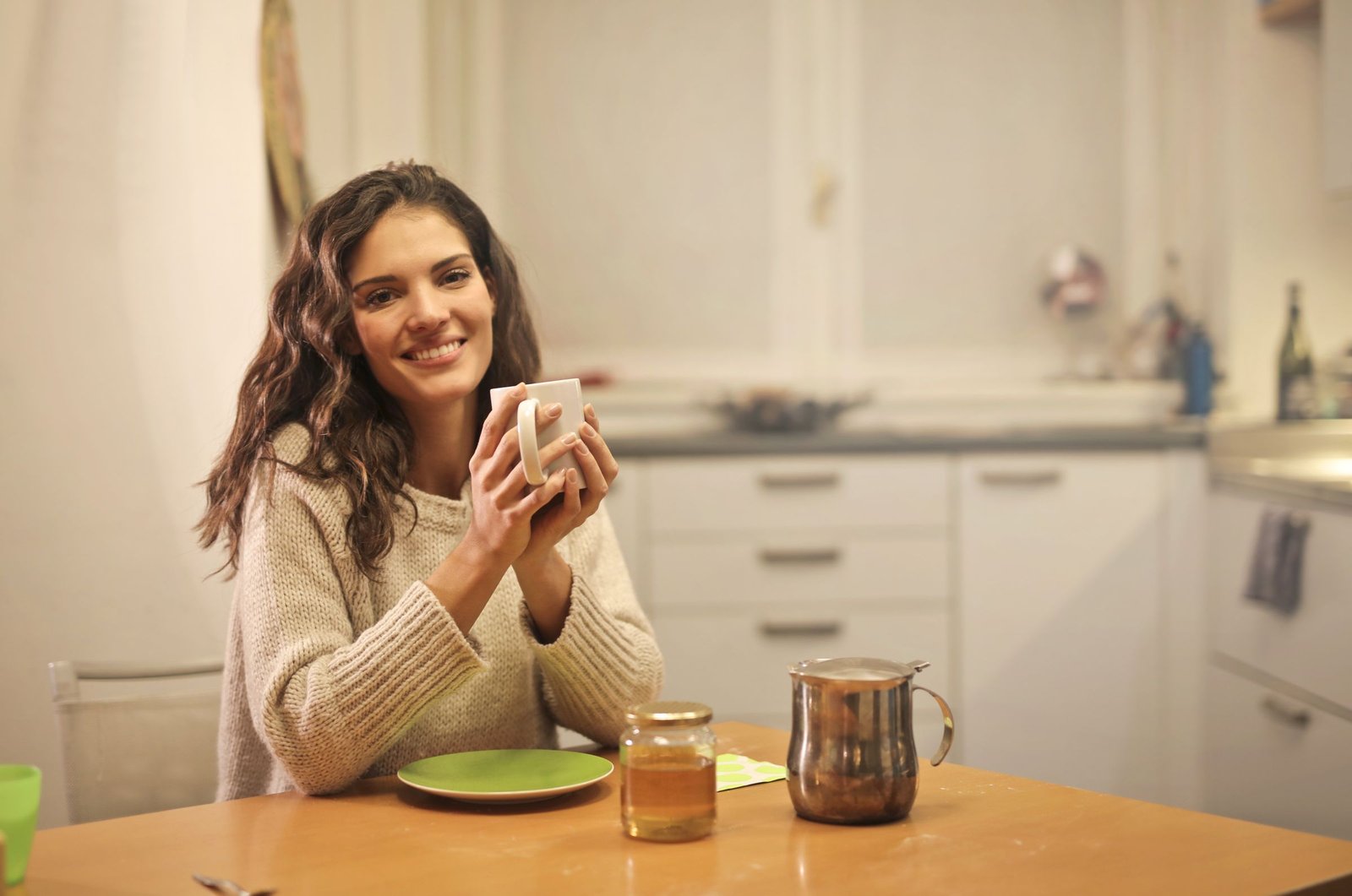 A woman smiling with a warm drink at home